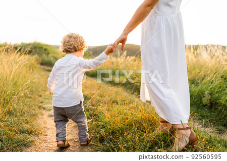 Little boy walking in nature holding his mother's hand Little boy walking in nature holding his mother's hand 92560595
