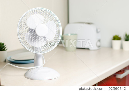 A small fan on the kitchen table. The concept of cooling and ventilation of the house. 92560842