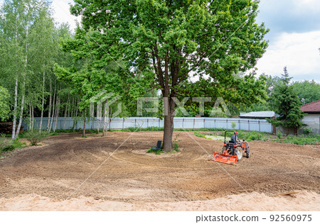 A man on a mini-excavator levels a piece of land, loosens the soil. 92560975