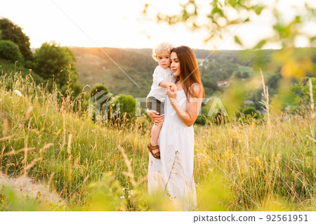 Mother walks with her son in arms in a picturesque summer field Mother walks with her son in arms in a picturesque summer field 92561951