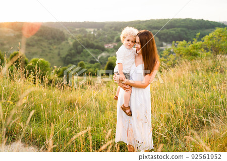 Mother and little son in nature. Beautiful woman in a summer dress walks with a child 92561952