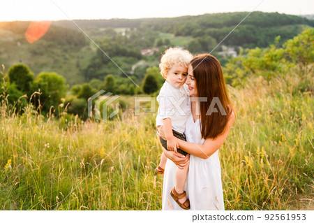 Happy mother loves her son. Woman with a boy in her arms are walking in nature Happy mother loves her son. Woman with a boy in her arms are walking in nature 92561953
