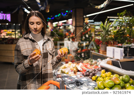 Young woman choosing exotic kiwano fruit in supermarket. Girl in the fruit department of a grocery store Young woman choosing exotic kiwano fruit in supermarket. Girl in the fruit department of a grocery store 92561974