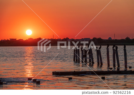 Beautiful red and orange sunset over the sea. The sun goes down over the sea. A flock of cormorants sits on a old sea pier in orange sunset light Beautiful red and orange sunset over the sea. The sun goes down over the sea. A flock of cormorants sits on a old sea pier in orange sunset light 92562216