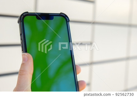 Female hand holding mobile phone with green screen chroma key next to Parcel locker Collecting parcel from shopping locker. Woman Skans QR Code on Mobile phone Self-service Locker Cell with Bar code 92562730