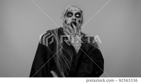 Frightening man Halloween zombie raising hands in surprise looking shocked by sudden victory 92563336