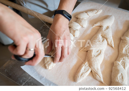 The process of making French traditional bread. Baguettes ear, notching the dough. Front view. 92568412