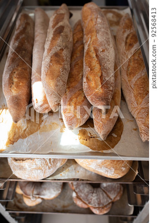 Finished French bread in the bakery on the racks. Baguettes, rustic bread, crown of kings Bordeaux. Vertical photo. Finished French bread in the bakery on the racks. Baguettes, rustic bread, crown of kings Bordeaux. Vertical photo. 92568413