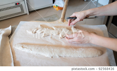The process of making French traditional bread. Baguettes ear, notching the dough. Front view. 92568416