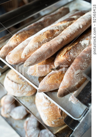 Finished French bread in the bakery on the racks. Baguettes, rustic bread, crown of kings Bordeaux. Vertical photo. Finished French bread in the bakery on the racks. Baguettes, rustic bread, crown of kings Bordeaux. Vertical photo. 92568418