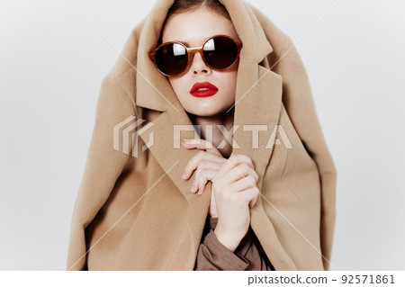 Conceptual catalog photography. A girl with glasses and a coat on her head poses on a white background 92571861