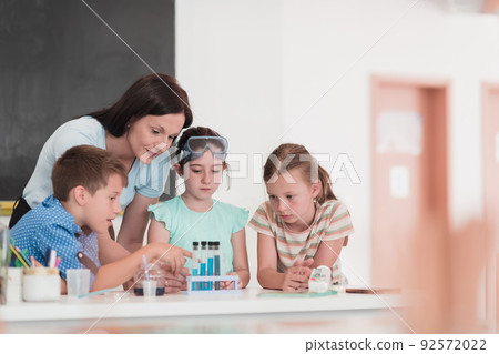 Elementary School Science Classroom: Enthusiastic Teacher Explains Chemistry to Diverse Group of Children, Little Boy Mixes Chemicals in Beakers. Children Learn with Interest Elementary School Science Classroom: Enthusiastic Teacher Explains Chemistry to Diverse Group of Children, Little Boy Mixes Chemicals in Beakers. Children Learn with Interest 92572022