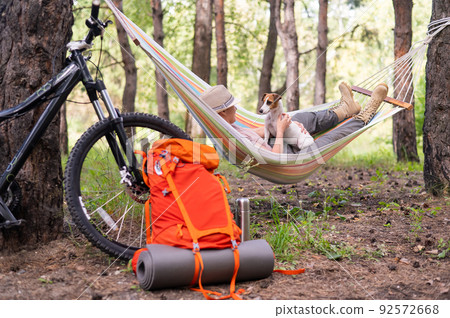 Caucasian woman lies in a hammock with Jack Russell Terrier dog in a pine forest 92572668