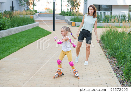 Caucasian woman teaches her daughter to skate on roller skates. Caucasian woman teaches her daughter to skate on roller skates. 92572995