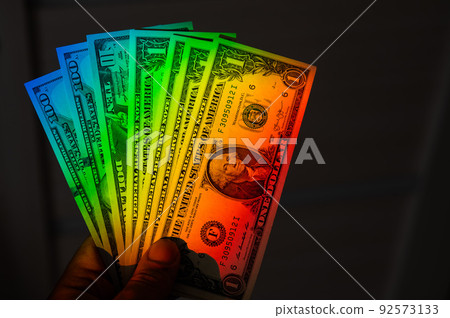Rays of a rainbow on a man's hand with a bundle of dollars.  92573133