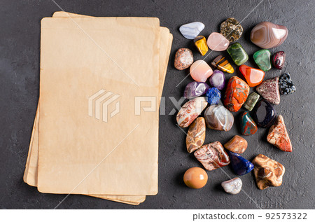 Mineral stones and an old piece of paper. Black concrete background. The concept of using minerals in astrology and alternative medicine. Copy space. 92573322