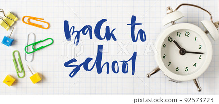 Back to school. Handwritten inscription. School supplies on white checkered paper Back to school. Handwritten inscription. School supplies on white checkered paper 92573723