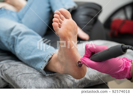 A pedicurist treats the heels of a client using a machine with an abrasive disc in a beauty salon. A pedicurist treats the heels of a client using a machine with an abrasive disc in a beauty salon. 92574018