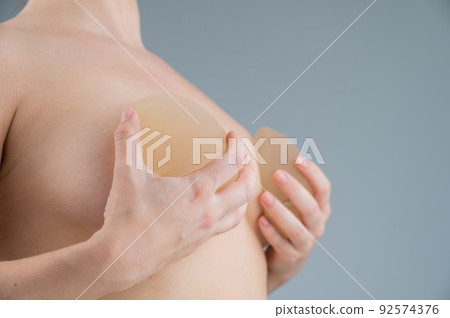 Caucasian naked woman trying on silicone breast implants on a white background. Caucasian naked woman trying on silicone breast implants on a white background. 92574376