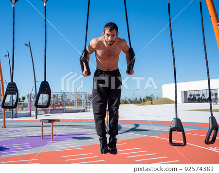 Shirtless man doing loop exercises outdoors. Shirtless man doing loop exercises outdoors. 92574381