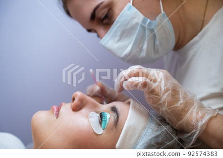 The master removes the composition for lamination from the client's eyelashes with a cotton swab. Eyelash perm procedure. The master removes the composition for lamination from the client's eyelashes with a cotton swab. Eyelash perm procedure. 92574383