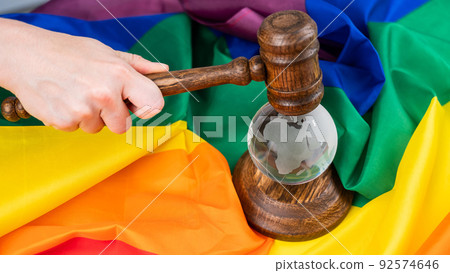 Woman judge holding a gavel on a crystal globe on a rainbow flag. LGBT community. 92574646