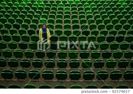 A caucasian woman stands on an empty tribune of a stadium. Female cheerleader. A caucasian woman stands on an empty tribune of a stadium. Female cheerleader. 92574657