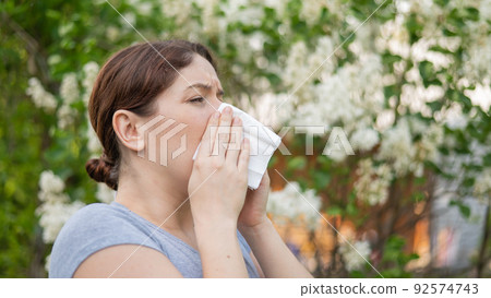 Caucasian woman suffers from allergies and blows her nose into a napkin while walking in the park.  92574743
