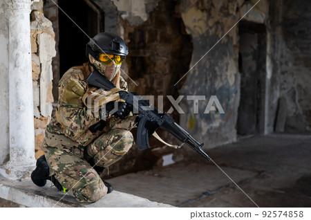 Portrait of a woman in a helmet and goggles with a machine gun in her hands. A female soldier in a camouflage uniform holds a weapon. Portrait of a woman in a helmet and goggles with a machine gun in her hands. A female soldier in a camouflage uniform holds a weapon. 92574858