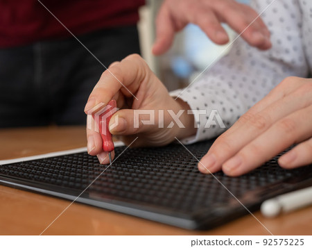 A man teaches a woman how to use a special stencil and stylus to write a letter in Braille. A man teaches a woman how to use a special stencil and stylus to write a letter in Braille. 92575225