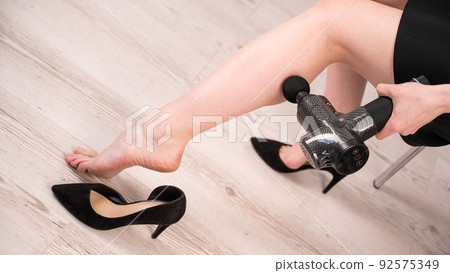 Caucasian business woman massaging her leg with a percussion massager. 92575349