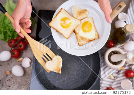 Fried egg Toasts with heart shaped holes on frying pan 92575373