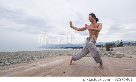 Caucasian man with naked torso practicing wushu on the seashore.  92575401
