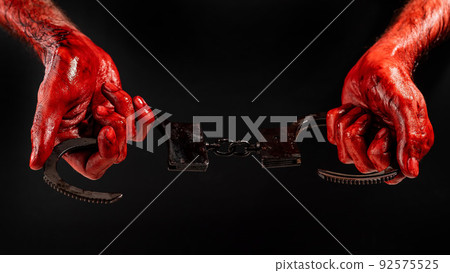 A man with bloody hands holds iron handcuffs. 92575525