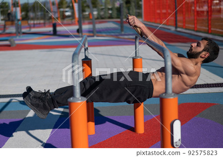 Shirtless man doing horizontal balance on parallel bars at sports ground.  92575823