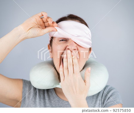 Caucasian woman yawns with travel pillow and sleep mask on white background. 92575850