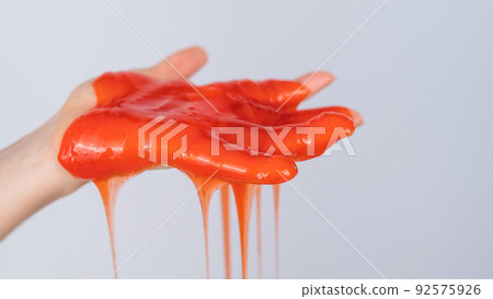 Red slime flowing down from a woman's hand on a white background. Red slime flowing down from a woman's hand on a white background. 92575926