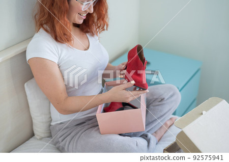 Caucasian woman opens ordered shoes while sitting in bed. Online shopping concept with home delivery 92575941
