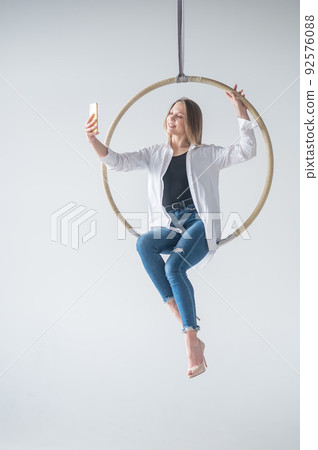 Caucasian woman gymnast on an aerial hoop takes a selfie on a smartphone.  92576088