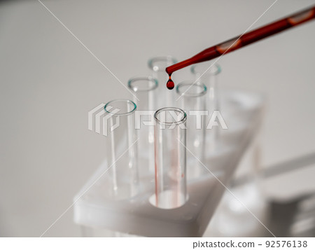 Close-up of a laboratory assistant dripping blood from a pipette into a test tube. Close-up of a laboratory assistant dripping blood from a pipette into a test tube. 92576138