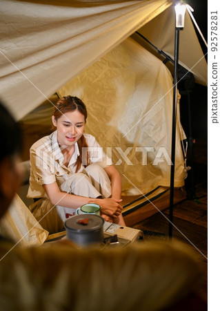 Happy Asian female camper sits in front of her tent and enjoy talking with her friends at night. 92578281