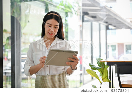 Gorgeous Asian businesswoman standing in the office and using portable tablet. 92578804