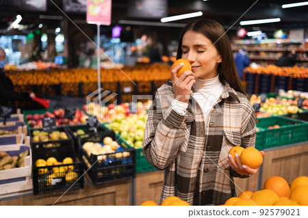 Female customer smelling orange in a supermarket. Woman chooses oranges. Girl at the fruit department of a grocery store Female customer smelling orange in a supermarket. Woman chooses oranges. Girl at the fruit department of a grocery store 92579021