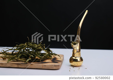 Close-up of cannabis leaves on a wooden board and smoke coming out of a pipe on a black background. Cannabis legalisation. 92580002