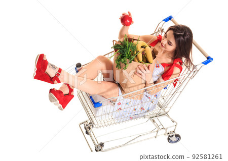 High angle view of girl smiling at camera while holding grocery bags and sitting in shopping trolley isolated on white High angle view of girl smiling at camera while holding grocery bags and sitting in shopping trolley isolated on white 92581261