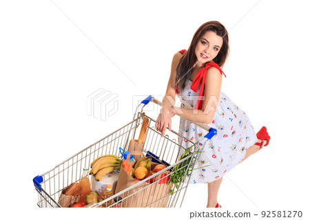 High angle view of girl smiling at camera while pushing a shopping cart full with groceries isolated on white background. High angle view of girl smiling at camera while pushing a shopping cart full with groceries isolated on white background. 92581270