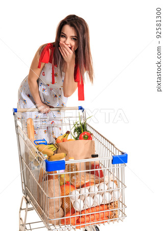 A young female pushing a shopping cart full with groceries isolated on white background. A woman laughs and closes her mouth with her palm 92581300