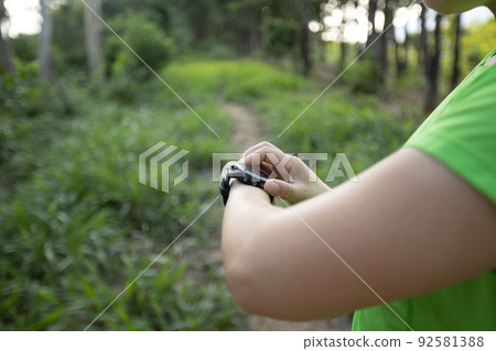 Woman trail runner set the sports watch in forest 92581388