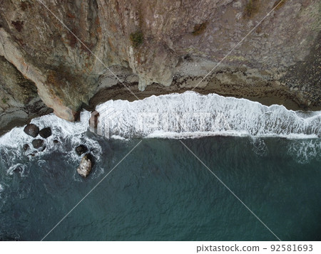 Aerial view from above on calm azure sea and volcanic rocky shores. Small waves on water surface in motion blur. Nature summer ocean sea beach background. Nobody. Holiday, vacation and travel concept 92581693
