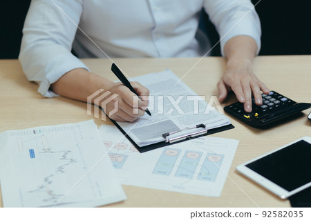 Close-up photo. The hands of a young man a male accountant in a white shirt who works at a desk with documents, a calculator, writes. Sitting in a modern office 92582035